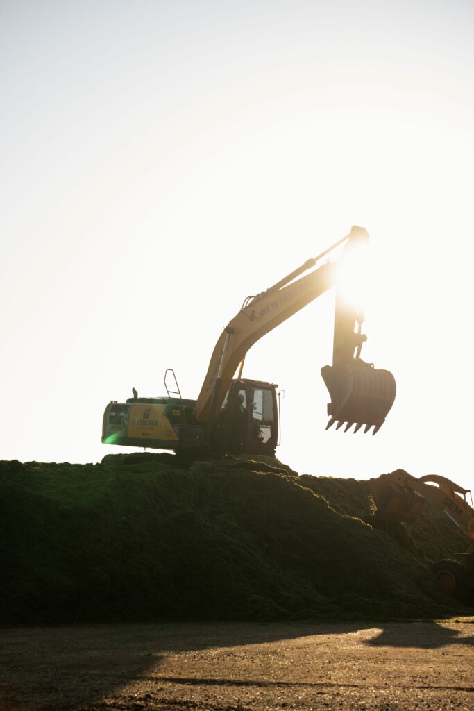 Services A silhouetted excavator works on a hill during a stunning sunset at a construction site.