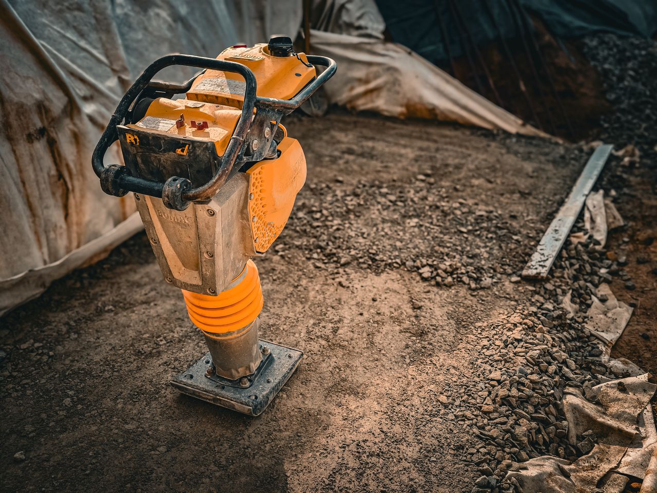Services Close-up of a vibratory compactor on a construction site with gravel and soil.